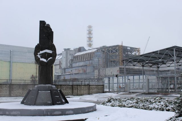Černobyl je plný pomníků. Tento z roku 2006 nesoucí nápis &quot;Těm,  kdo zachránili svět&quot; stojí hned před tzv. starým sarkofágem  (budova v pozadí),  pod nímž je pohřben havarovaný 4. blok | foto: Tomáš Zelenka