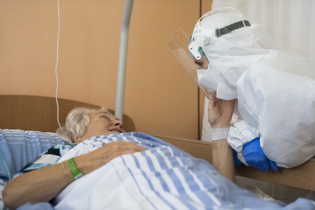 Pracovník v ochranném obleku,  který má kvůli koronaviru,  si povídá se seniorkou | foto: Ondřej Deml,  ČTK