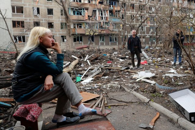 Lidé sedí před zničenými domy v Mariupolu | foto: Alexander Ermochenko,  Reuters