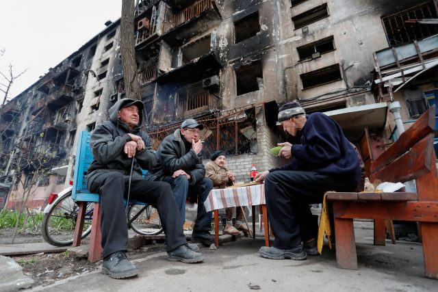 Obyvatelé Mariupolu sedí před zničenou budovou | foto: Reuters