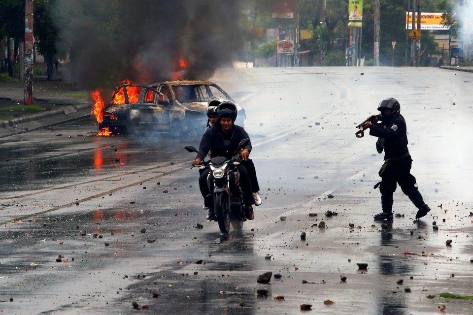 Policista míří zbraní na muže na motorce během protestů proti nikaragujskému prezidentovi Danielu Ortegovi | foto: Reuters