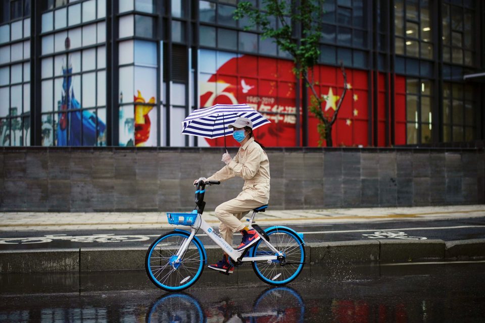 Žena projíždí na sdíleném kole kolem čínské vlajky | foto: Reuters