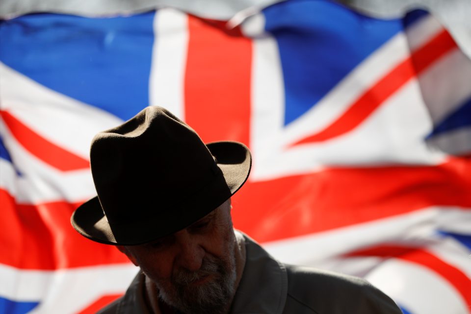 Muž stojící před britskou vlajku před budovou parlamentu. | foto: Peter Nicholls,  Reuters